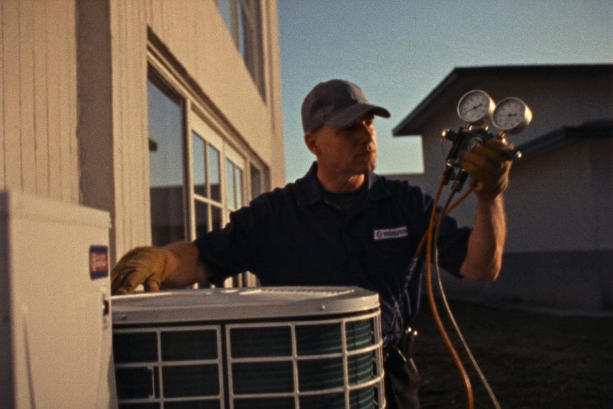 An HVAC technician servicing a condenser unit beside a home