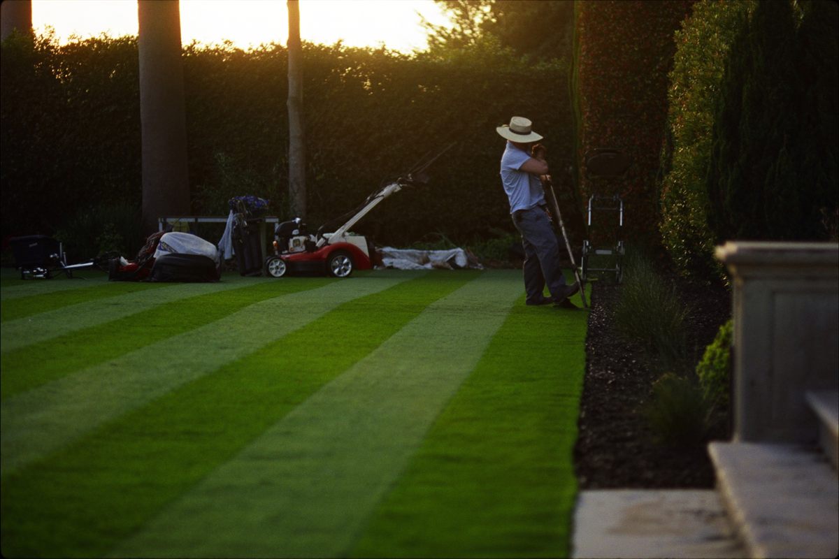 A landscaper mowing a striped lawn on an upscale property at golden hour