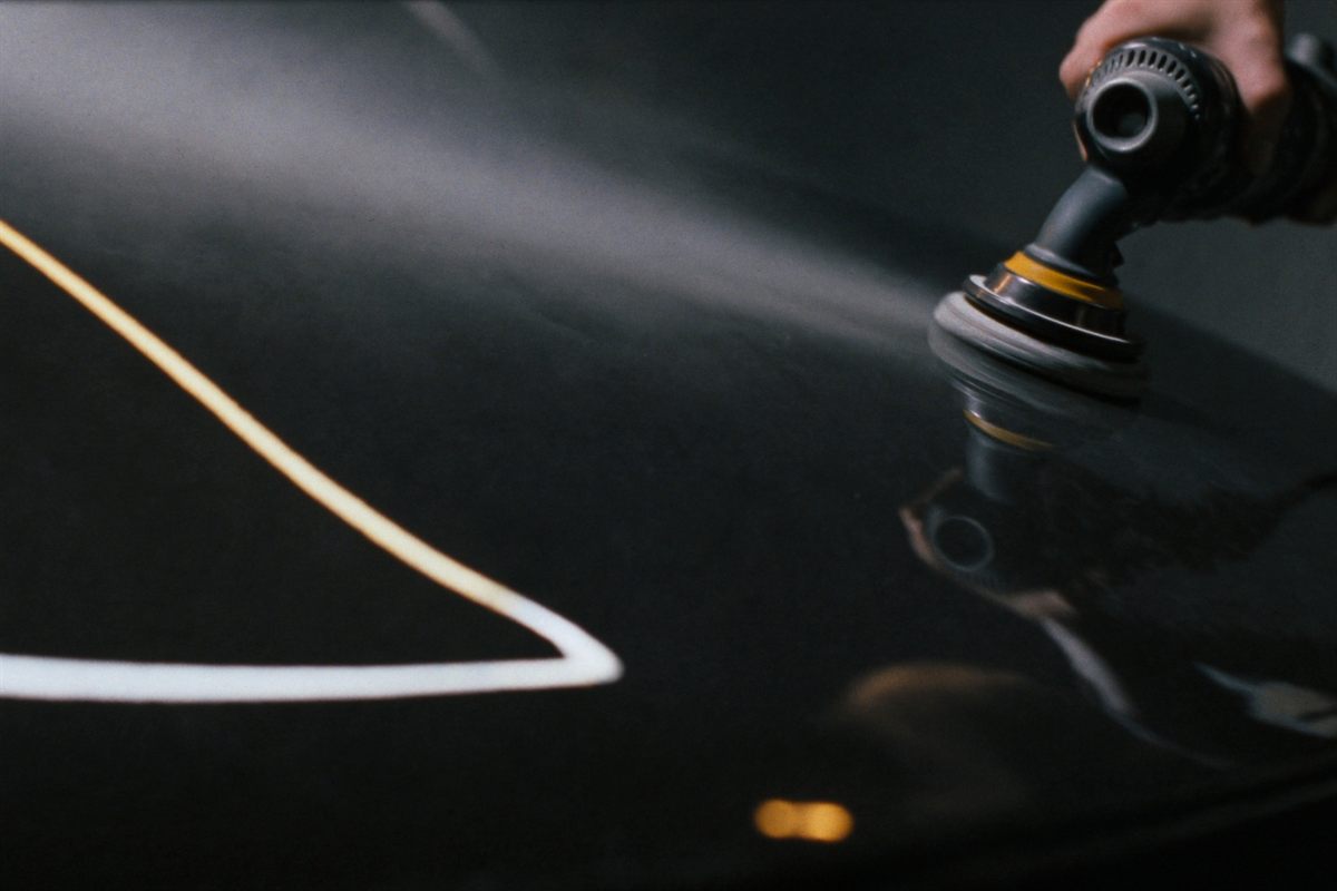 A dual-action polisher correcting paint on a dark car hood