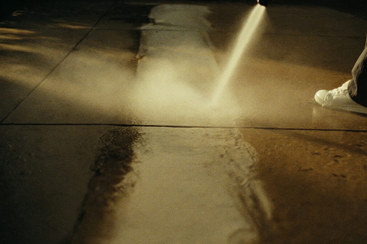 A pressure washer cutting a clean stripe across a dirty concrete driveway